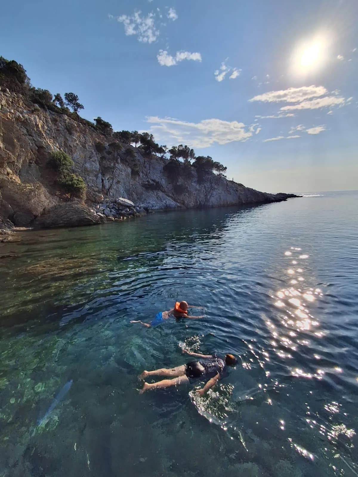 Two swimmers in the clear water of a quiet cove below the cliffs