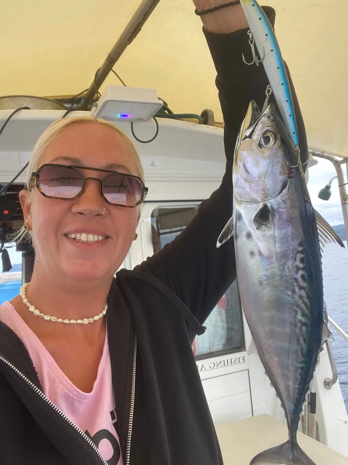 A crew member holding up a bonito under the boat awning