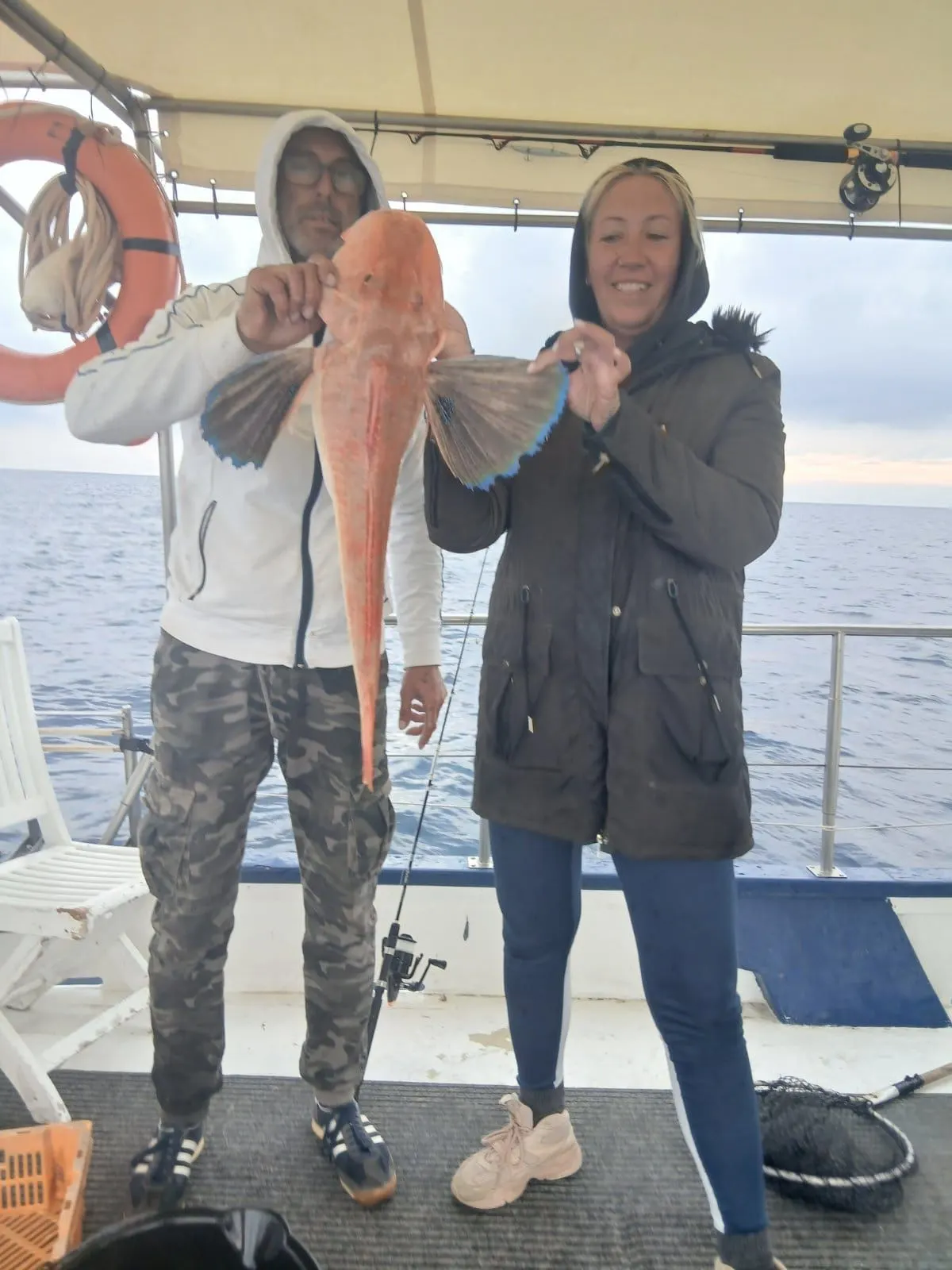 Dimitris and a crew member holding a tub gurnard with its blue fins spread